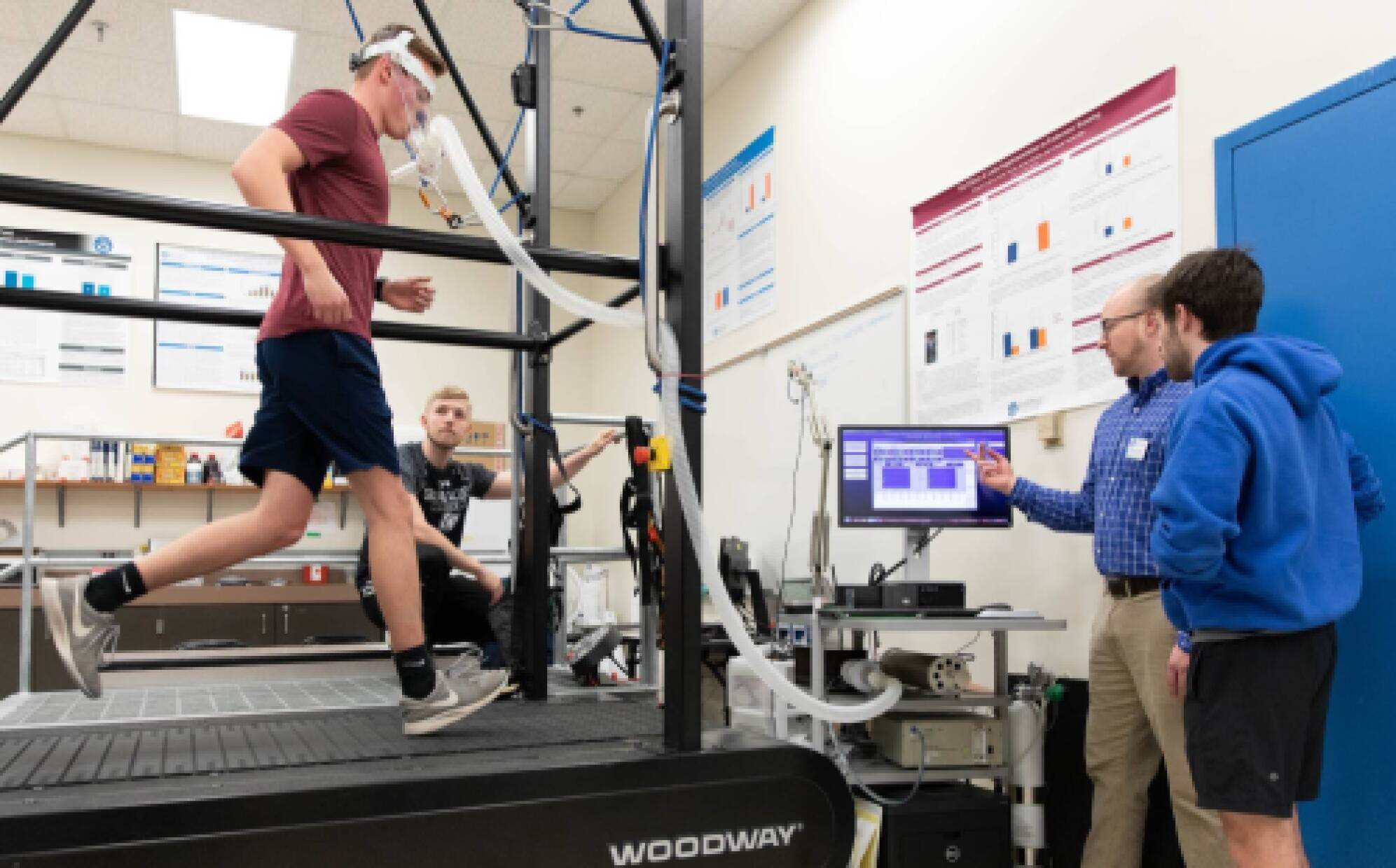 Student participating in exercise testing while faculty instructs another student on running the test.